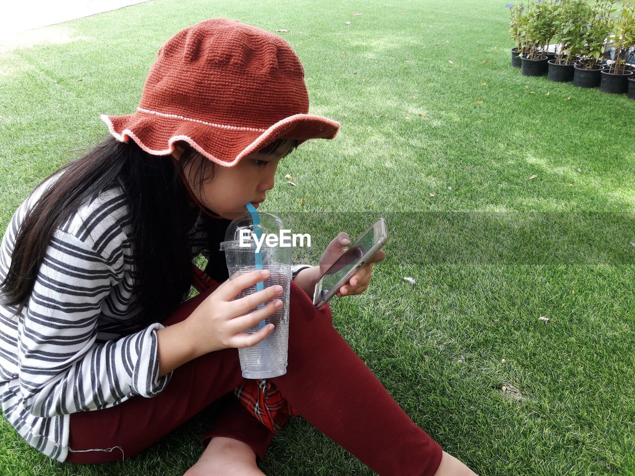 Girl drinking juice while using mobile phone on field