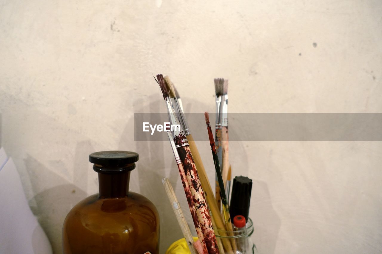 Close-up of paintbrushes in container by bottle against wall