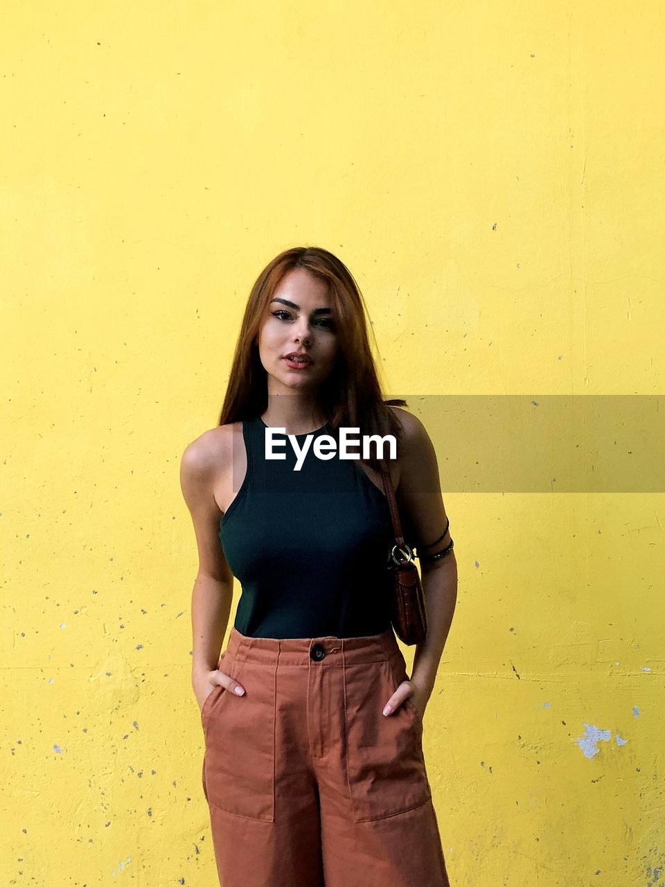 Portrait of beautiful young woman standing against yellow wall