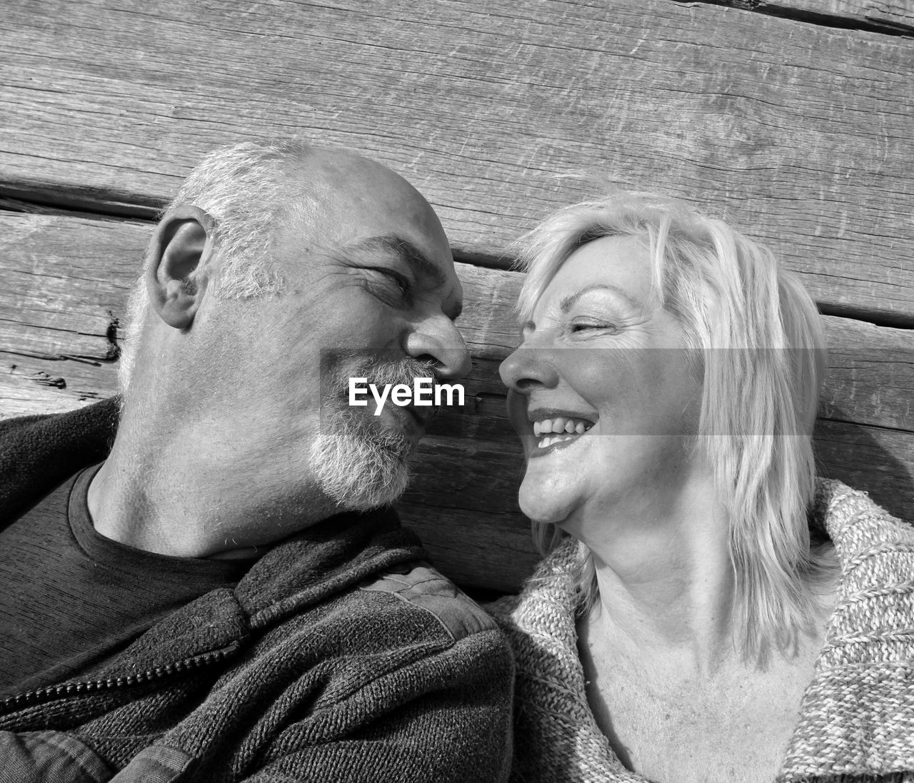 Happy senior couple looking at each other against wooden wall