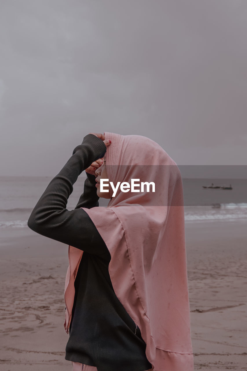 Midsection of woman standing on beach against sky