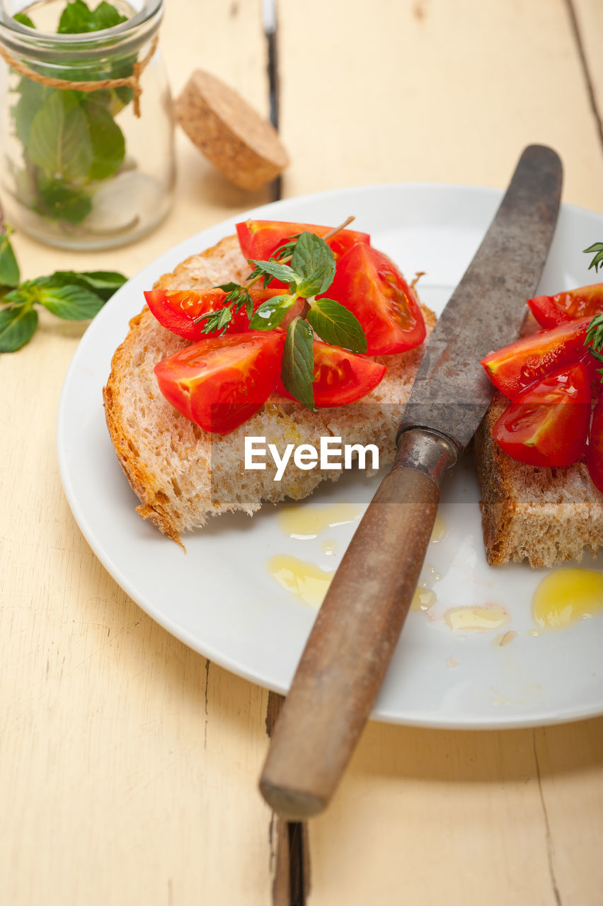 High angle view of tomato slices and herbs on breads in plate on table