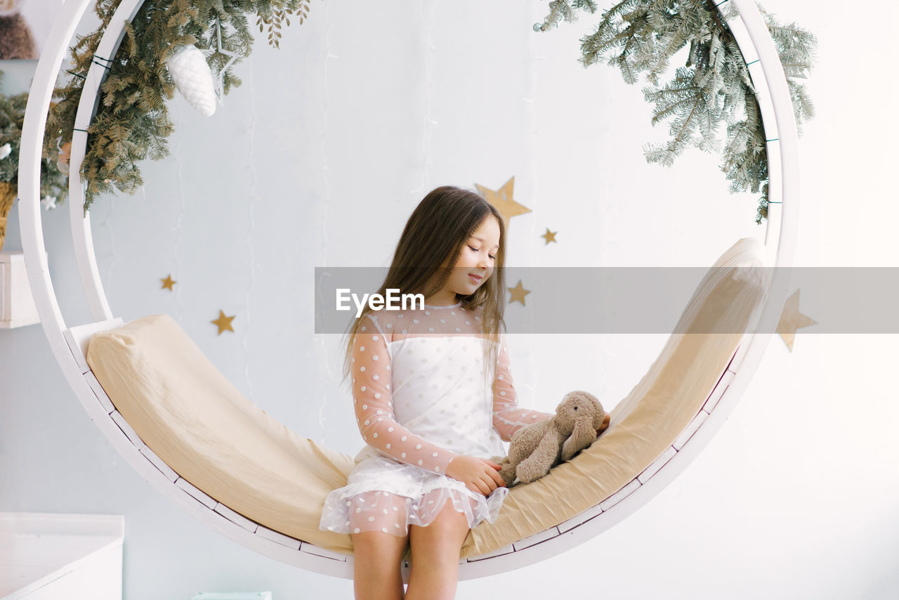 Cute girl holding a soft favorite toy and sitting on a swing decorated for christmas