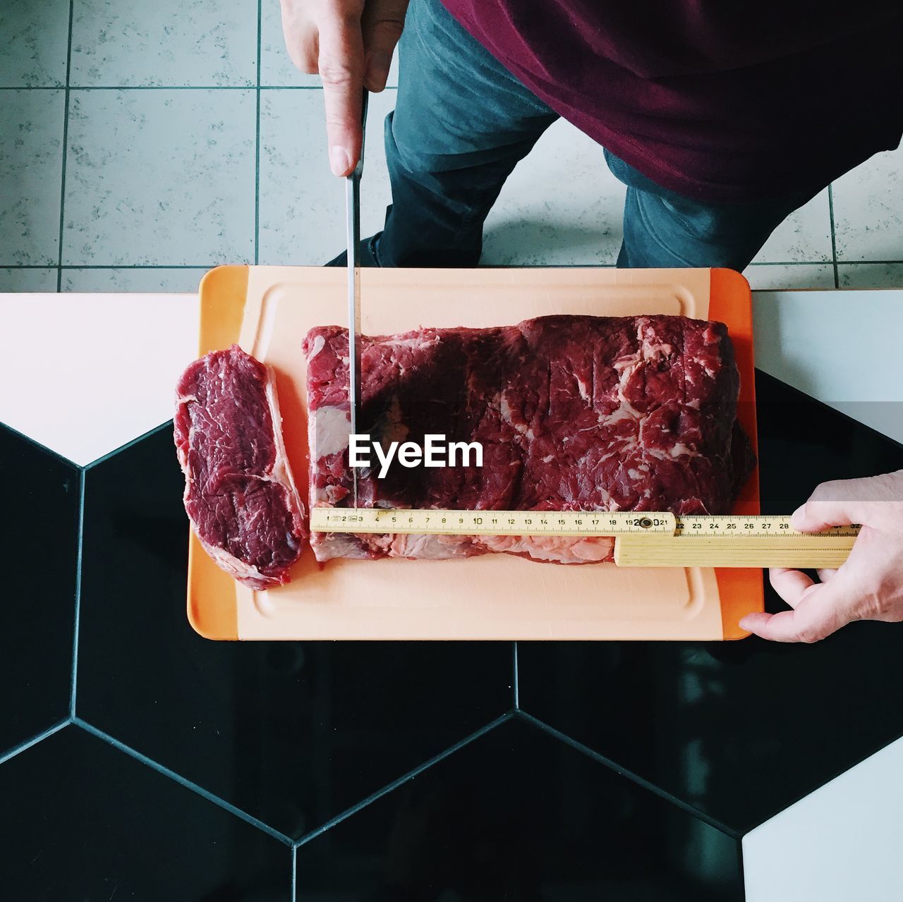 Low section of man cutting steak with measuring tape on table