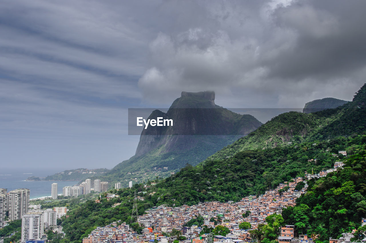 Cityscape by mountain against cloudy sky