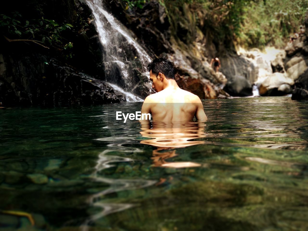 Rear view of shirtless man standing at waterfall