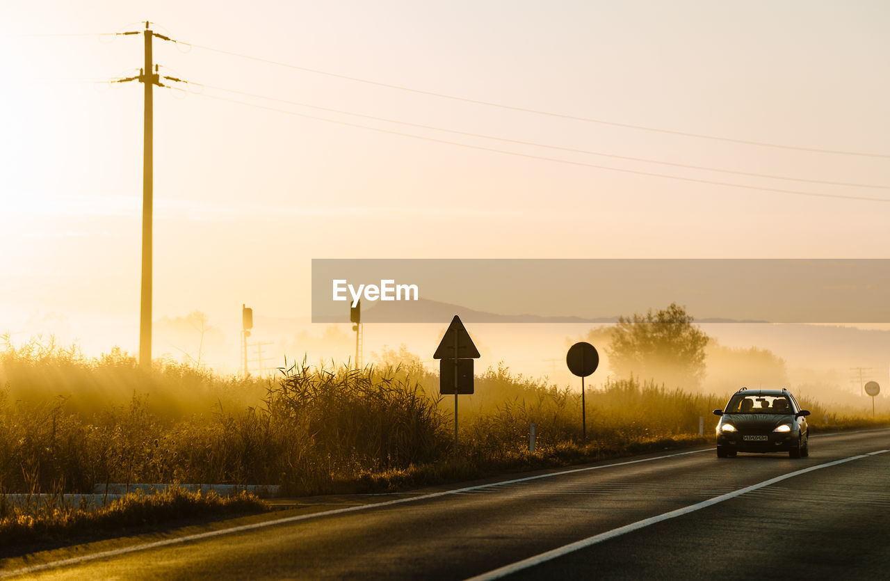 Car on road against sunrise sky during foggy summer morning