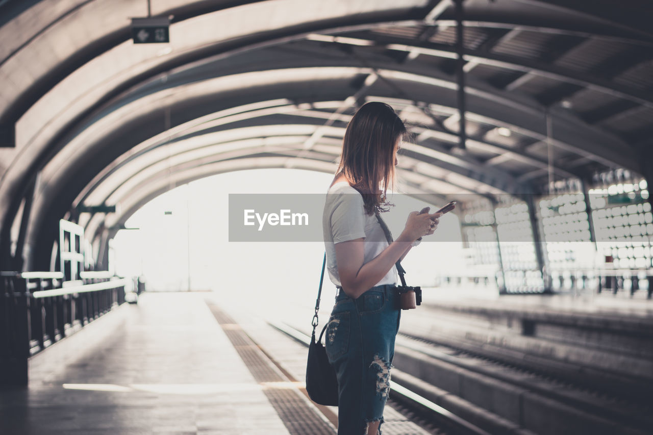 Side view of woman using mobile phone while standing at railroad station
