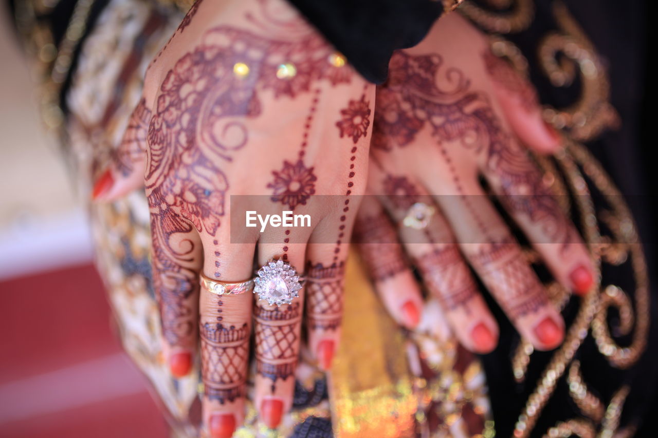 Midsection of woman hands with henna tattoo and diamond ring