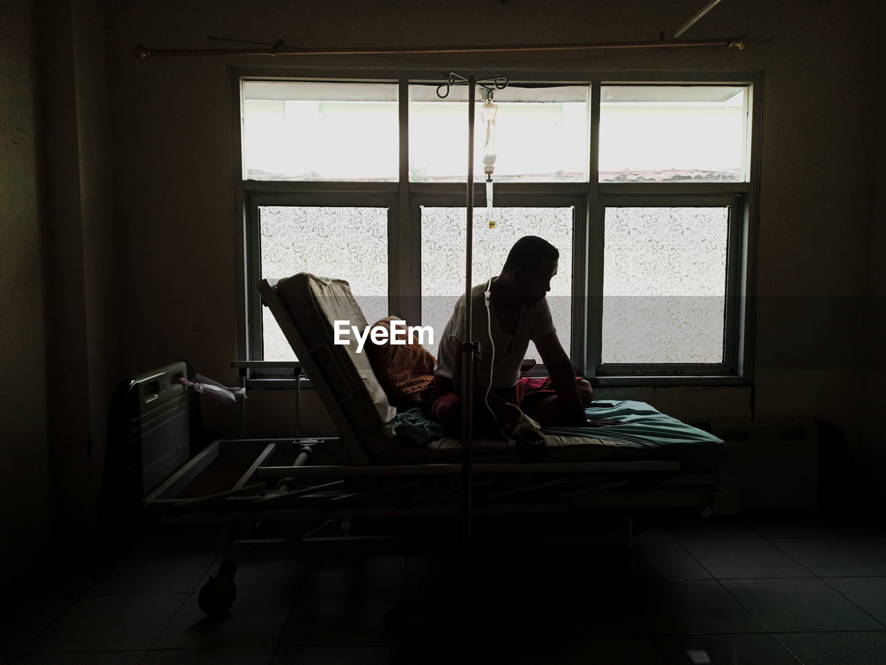 Rear view of man sitting on bed at hospital