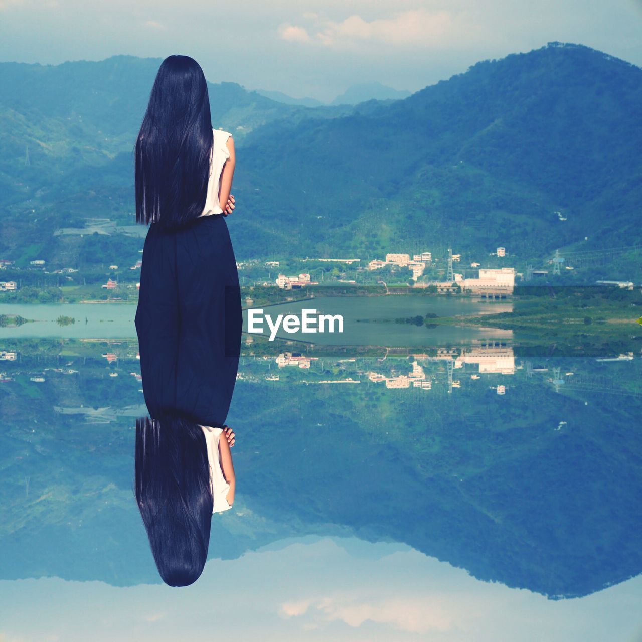 REAR VIEW OF WOMAN STANDING BY LAKE AGAINST MOUNTAIN