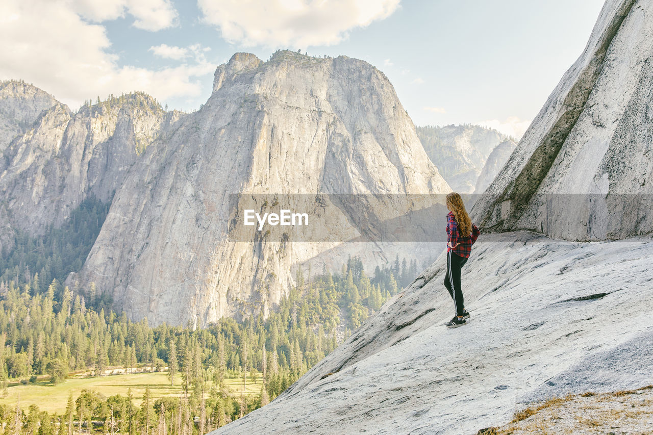 Young woman standing on el capitan mountain looking out to yosemite