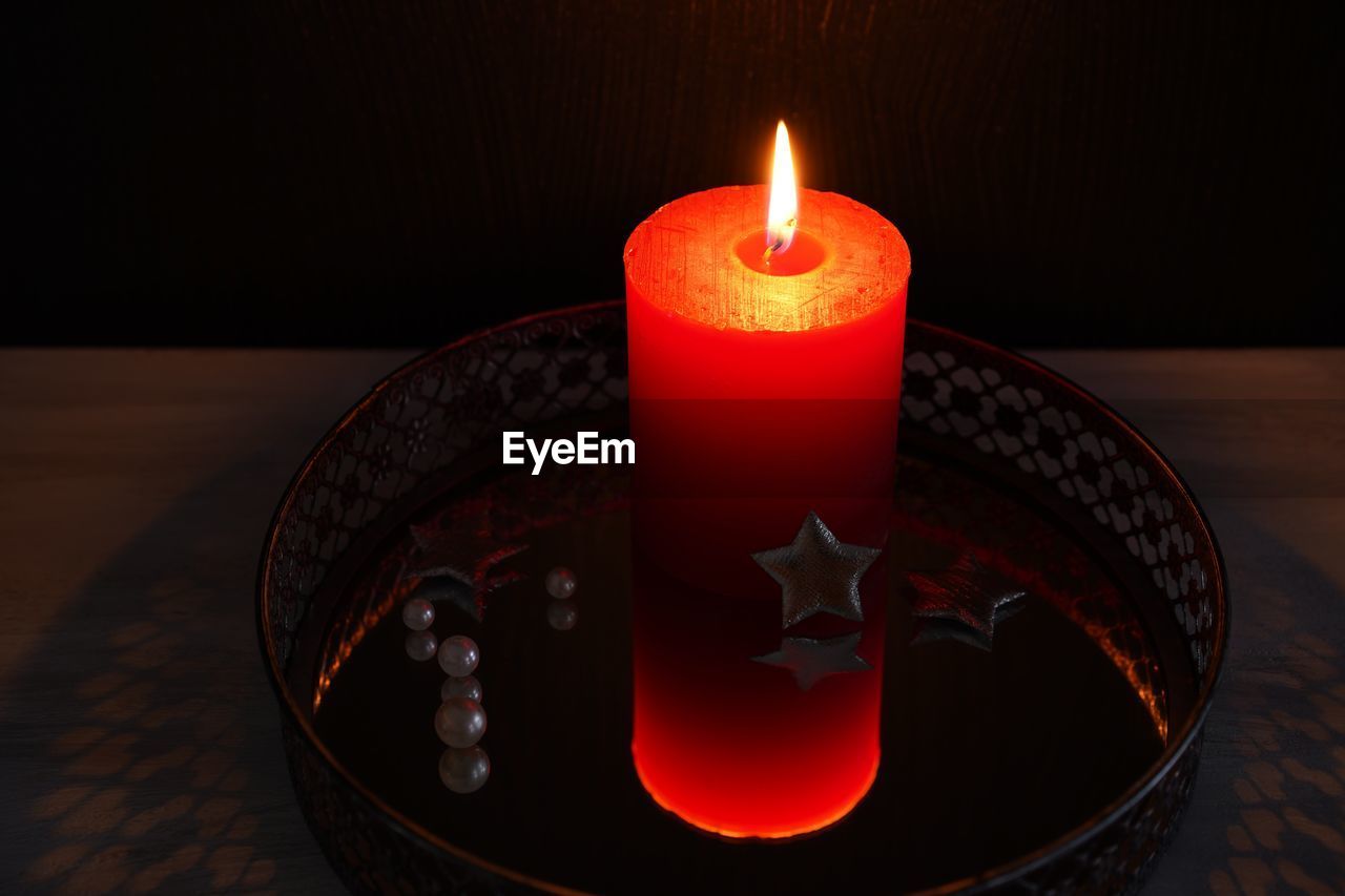 Close-up of illuminated red candle on mirror table