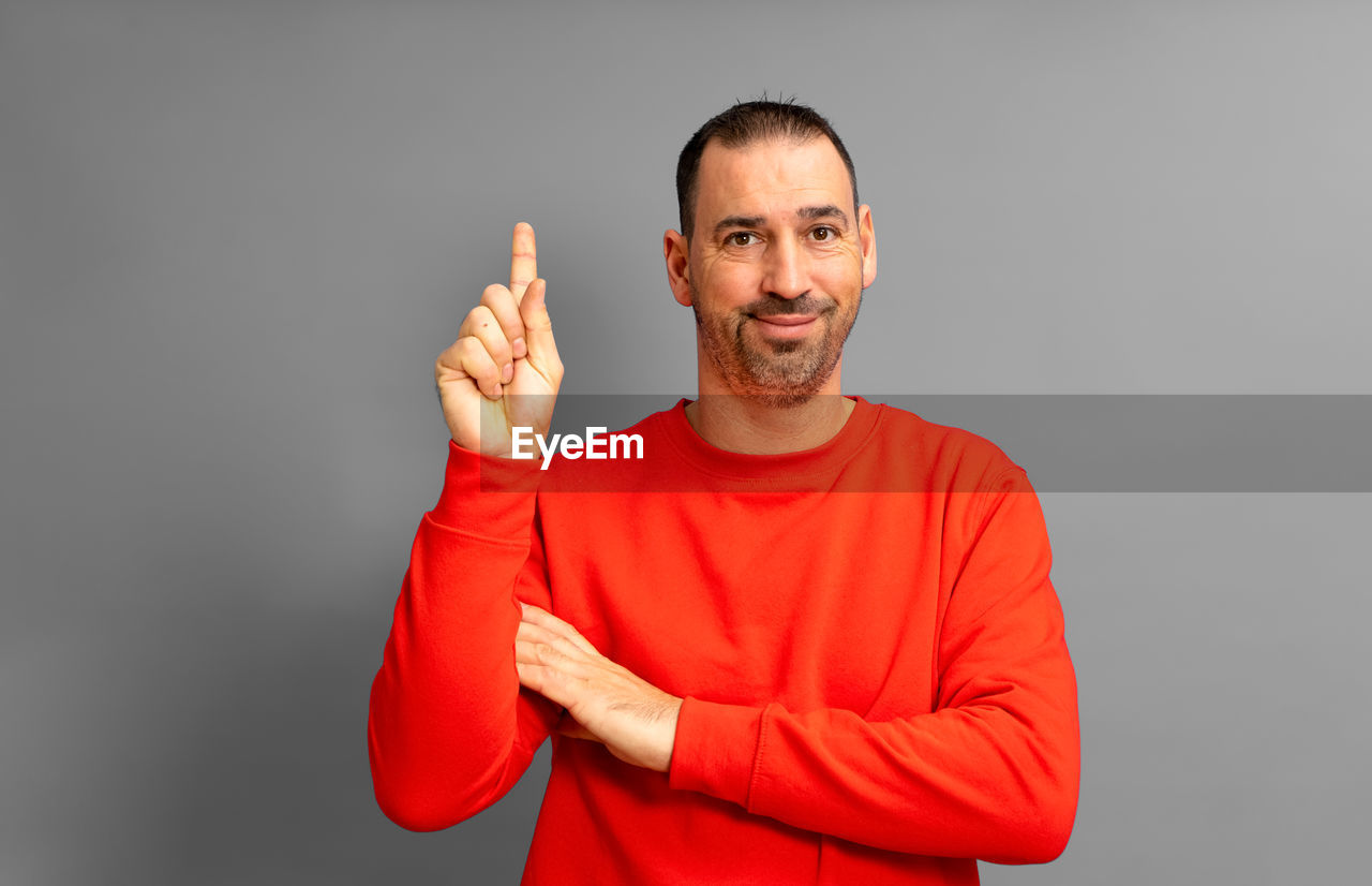 studio shot, one person, adult, portrait, men, smiling, looking at camera, person, indoors, happiness, emotion, waist up, gray background, gesturing, hand, gray, human face, clothing, beard, finger, positive emotion, red, arm, front view, facial hair, cheerful, casual clothing, thumbs up, standing, success, lifestyles, mature adult, sleeve, sign language, copy space, young adult