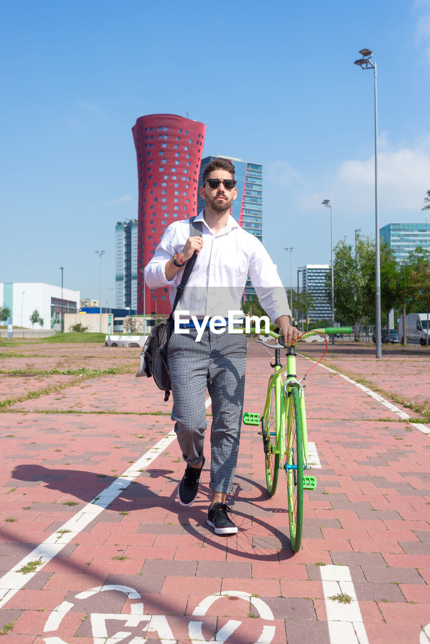 Bearded man in sunglasses walking with bike by bicycle track outdoors