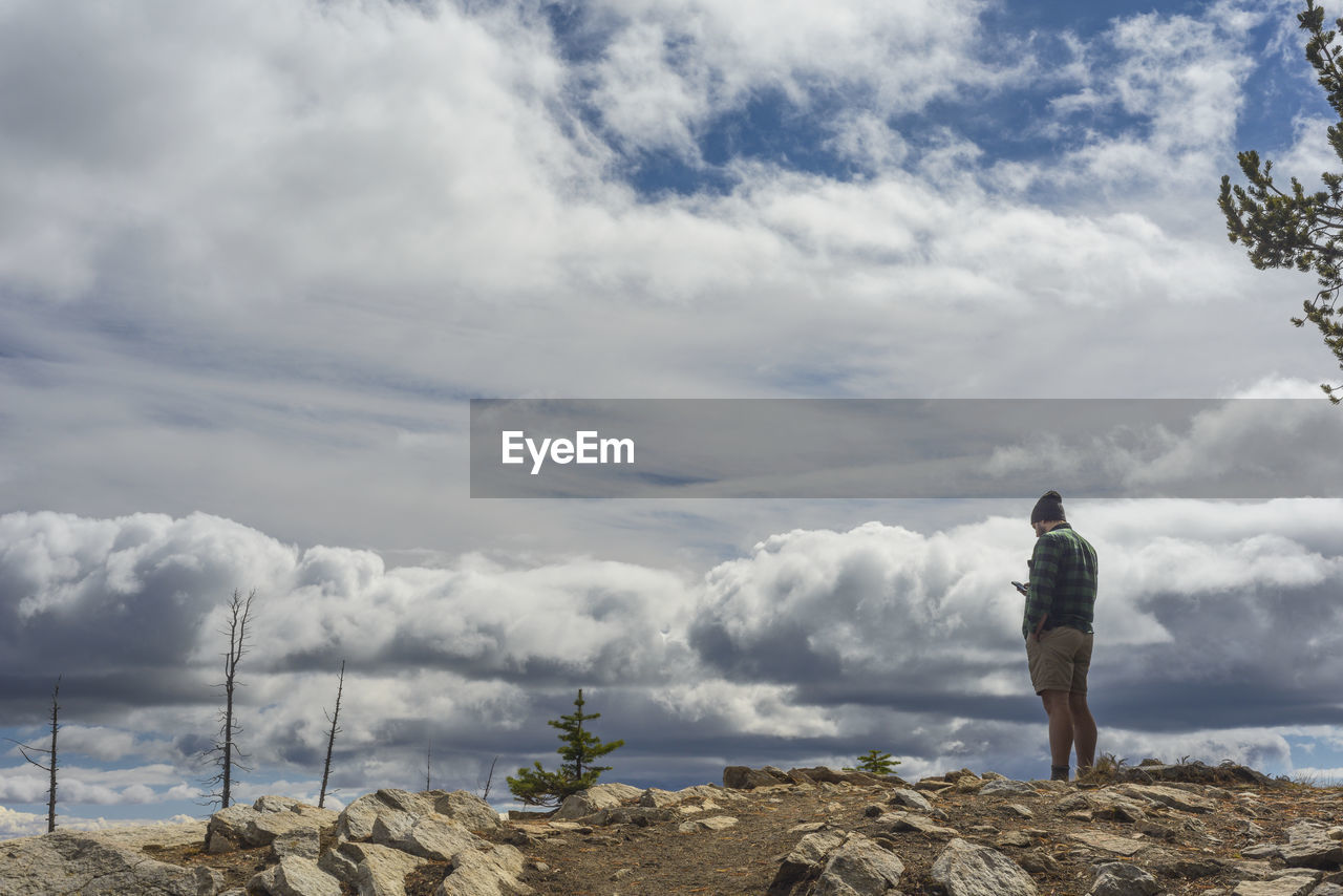 Male standing on mountain top looking at cell phone with moody clouds