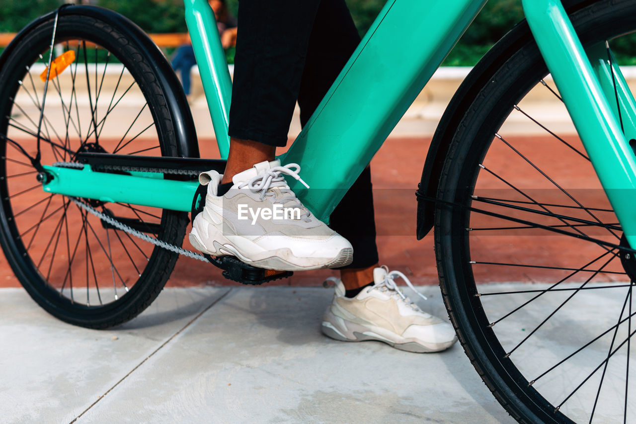 Crop unrecognizable ethnic male riding contemporary bike along street in city