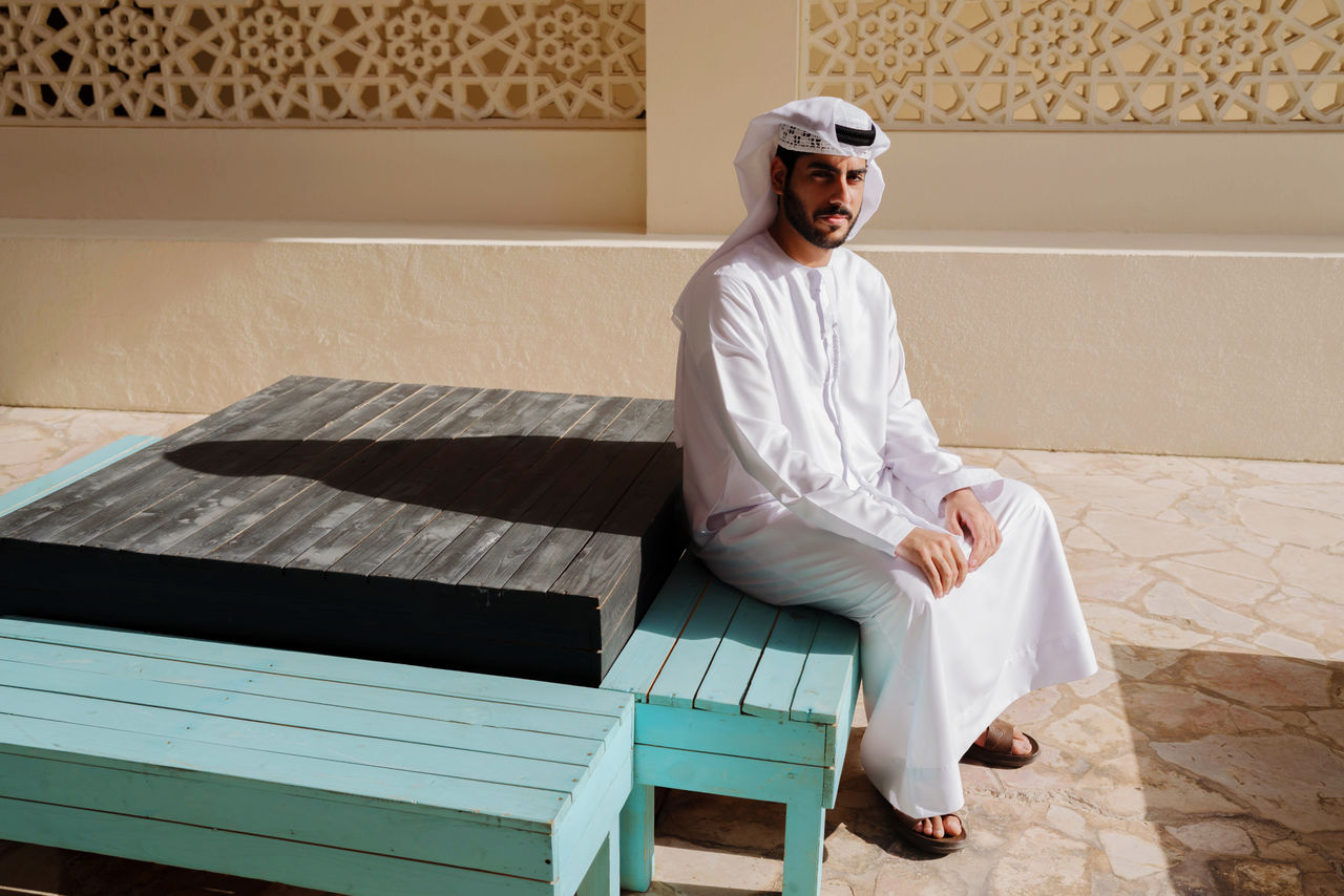 Portrait of arab man wearing dishdash kandura sitting down in a traditional bench