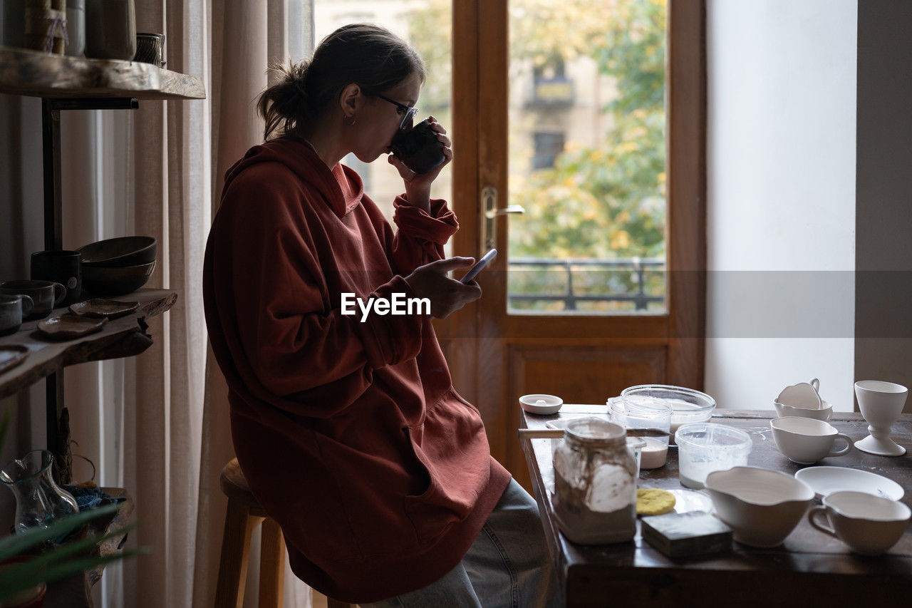 side view of young woman using mobile phone while standing in cafe