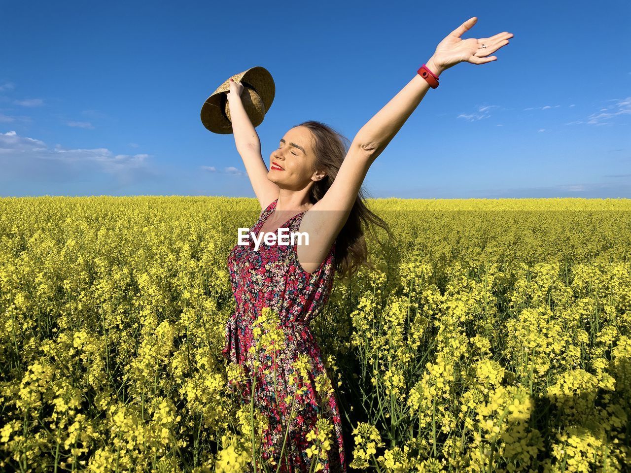 Happy woman wearing dress and hat in a field of canola flowers on a sunny day
