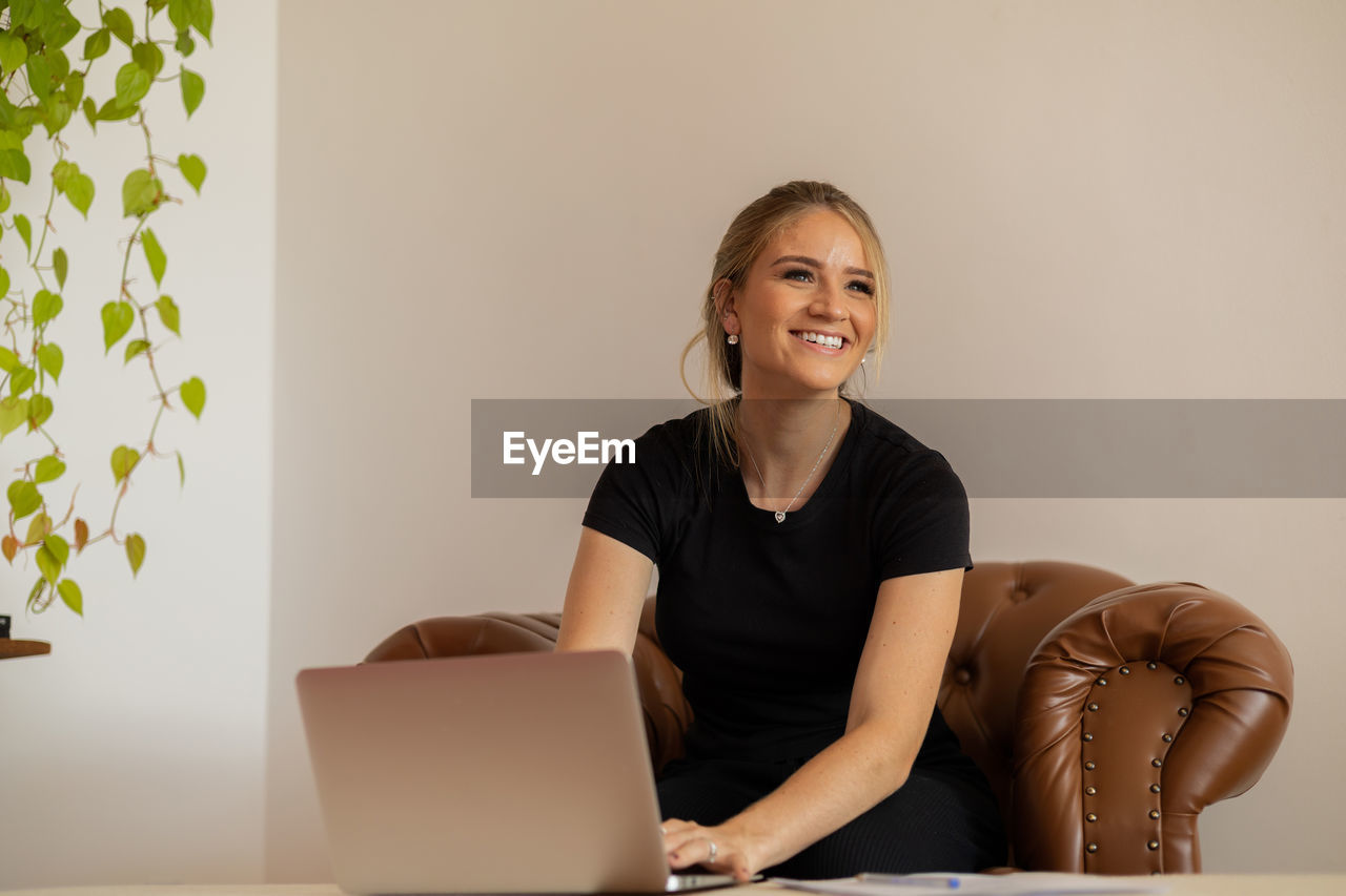 adult, laptop, one person, smiling, indoors, using laptop, computer, women, technology, wireless technology, happiness, portrait, sitting, business, communication, person, furniture, emotion, working, female, looking at camera, copy space, lifestyles, table, businesswoman, business finance and industry, cheerful, front view, internet, office, home interior, occupation, computer network, casual clothing, clothing, hairstyle, young adult, conversation, relaxation
