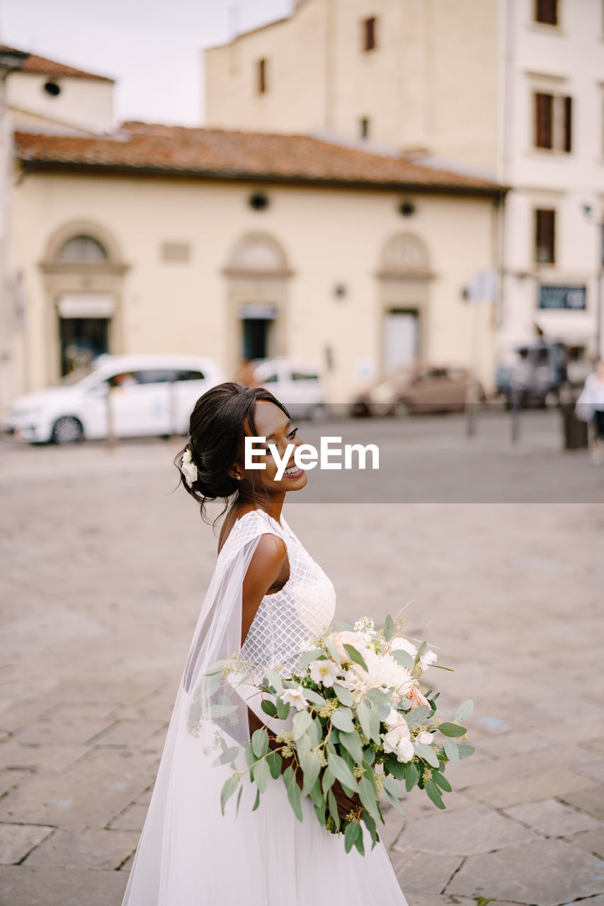 Side view of bride standing with flowering plant in city