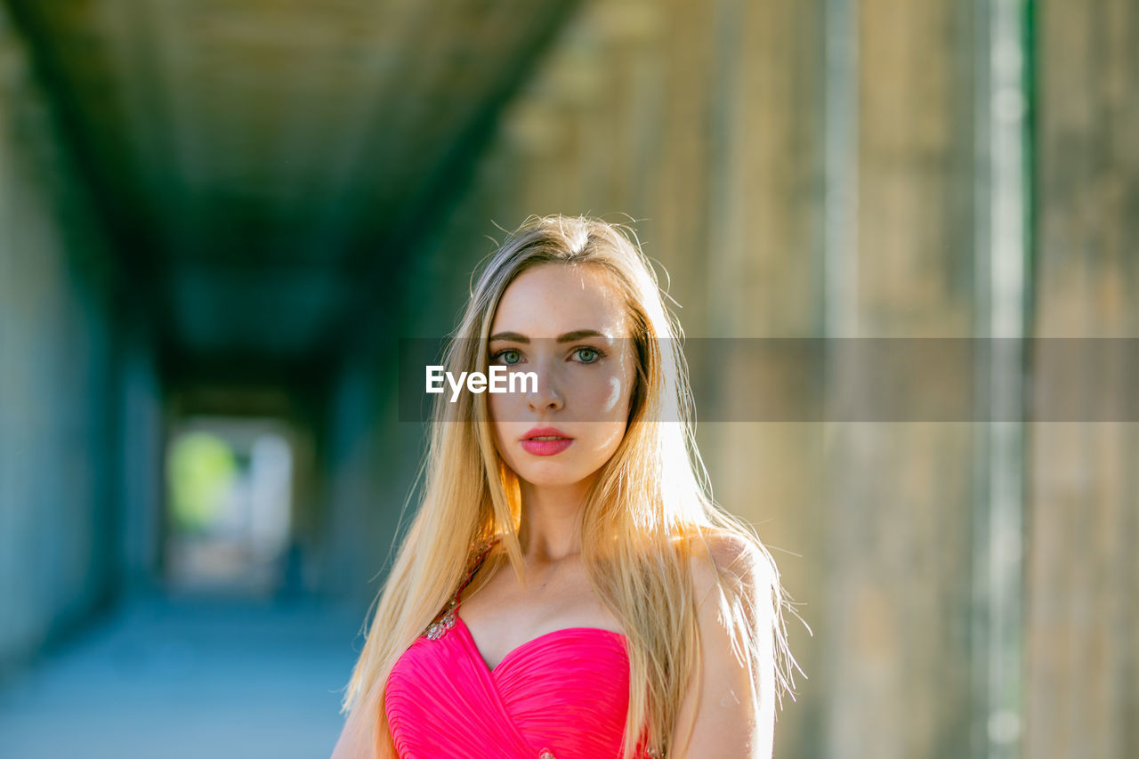 Close-up portrait of beautiful young woman in pink evening dress at colonnade