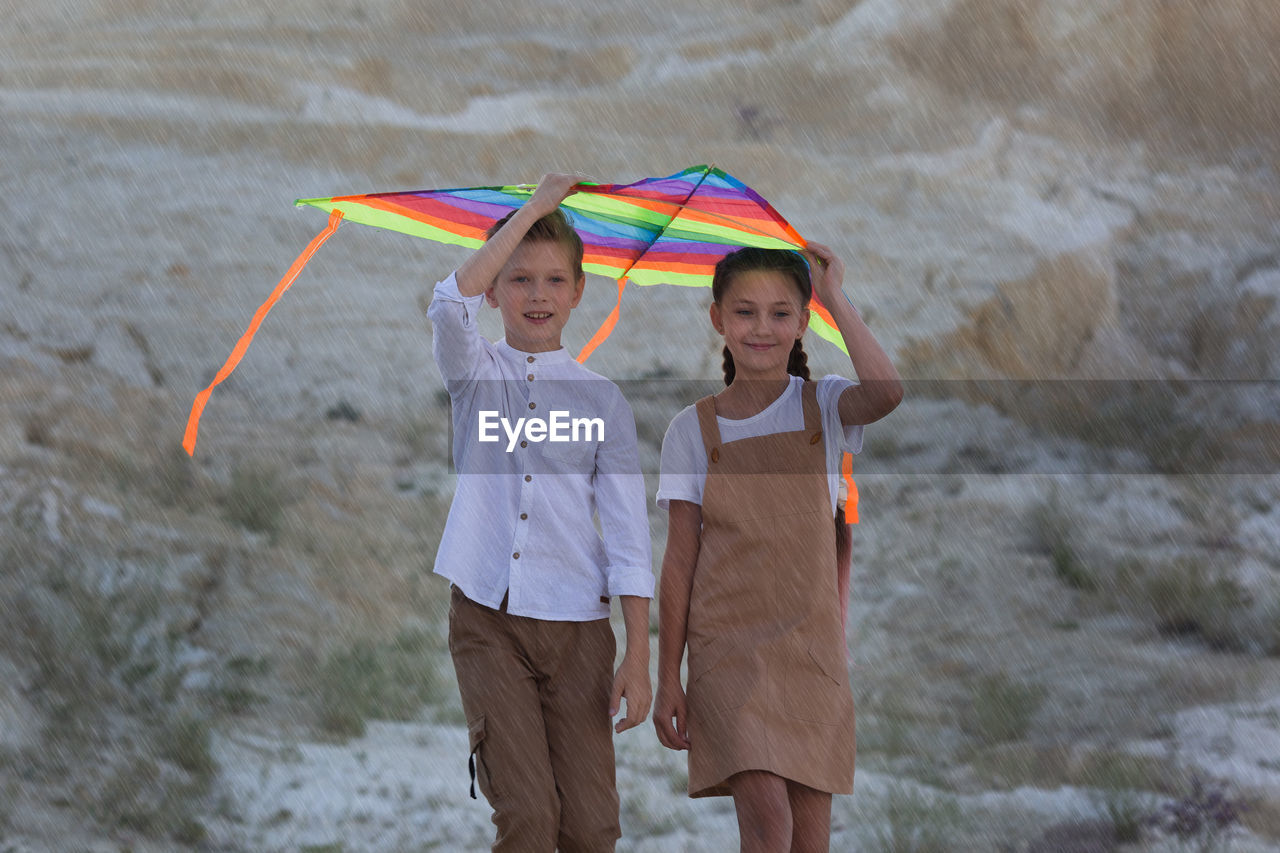 Children go sheltered from the rain with kite.