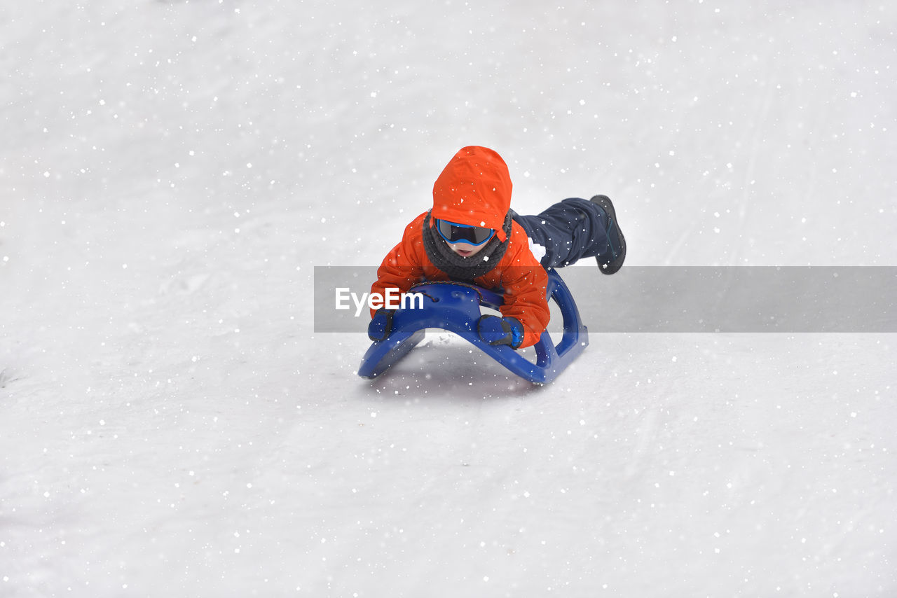 Full length of boy tobogganing on snowy field