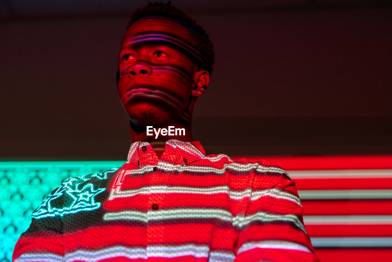 Serious african american male illuminated by red and blue neon projection of national american flag standing in dark studio