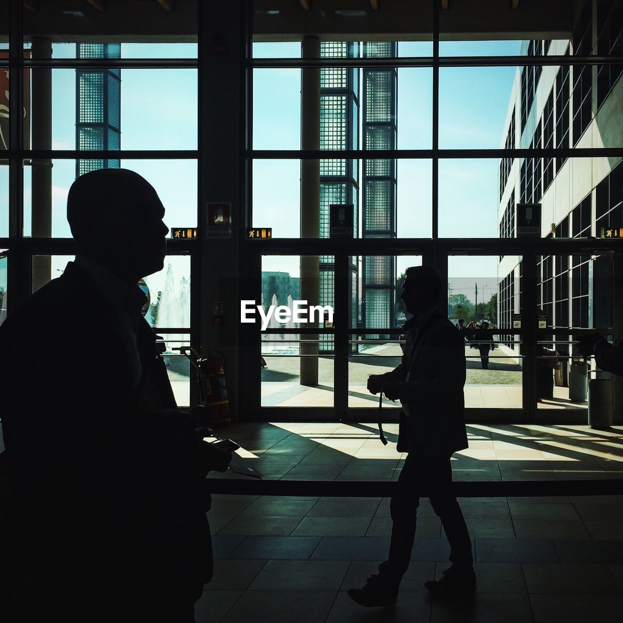 Silhouettes of two men walking in lobby of public building