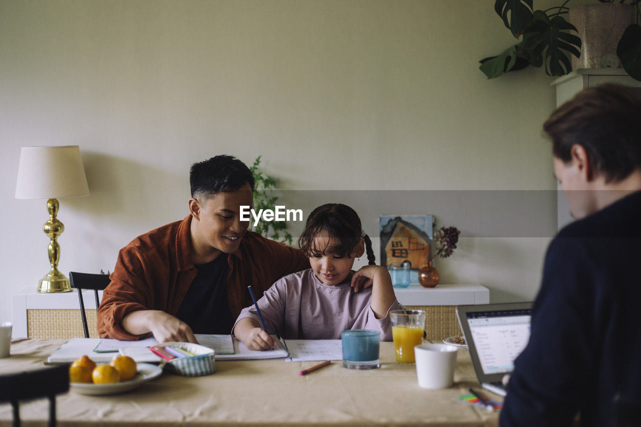 Gay father assisting daughter while doing homework at home