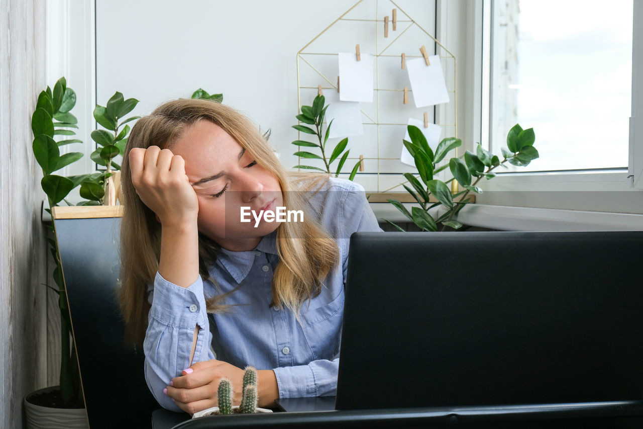 Tired sleepy young caucasian woman worker at desk workplace. overworking and sleeping deprivation. 