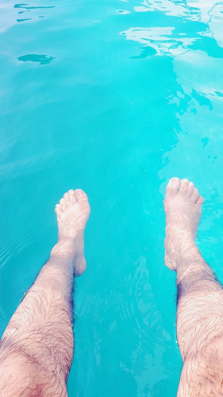 LOW SECTION OF MAN RELAXING ON SWIMMING POOL