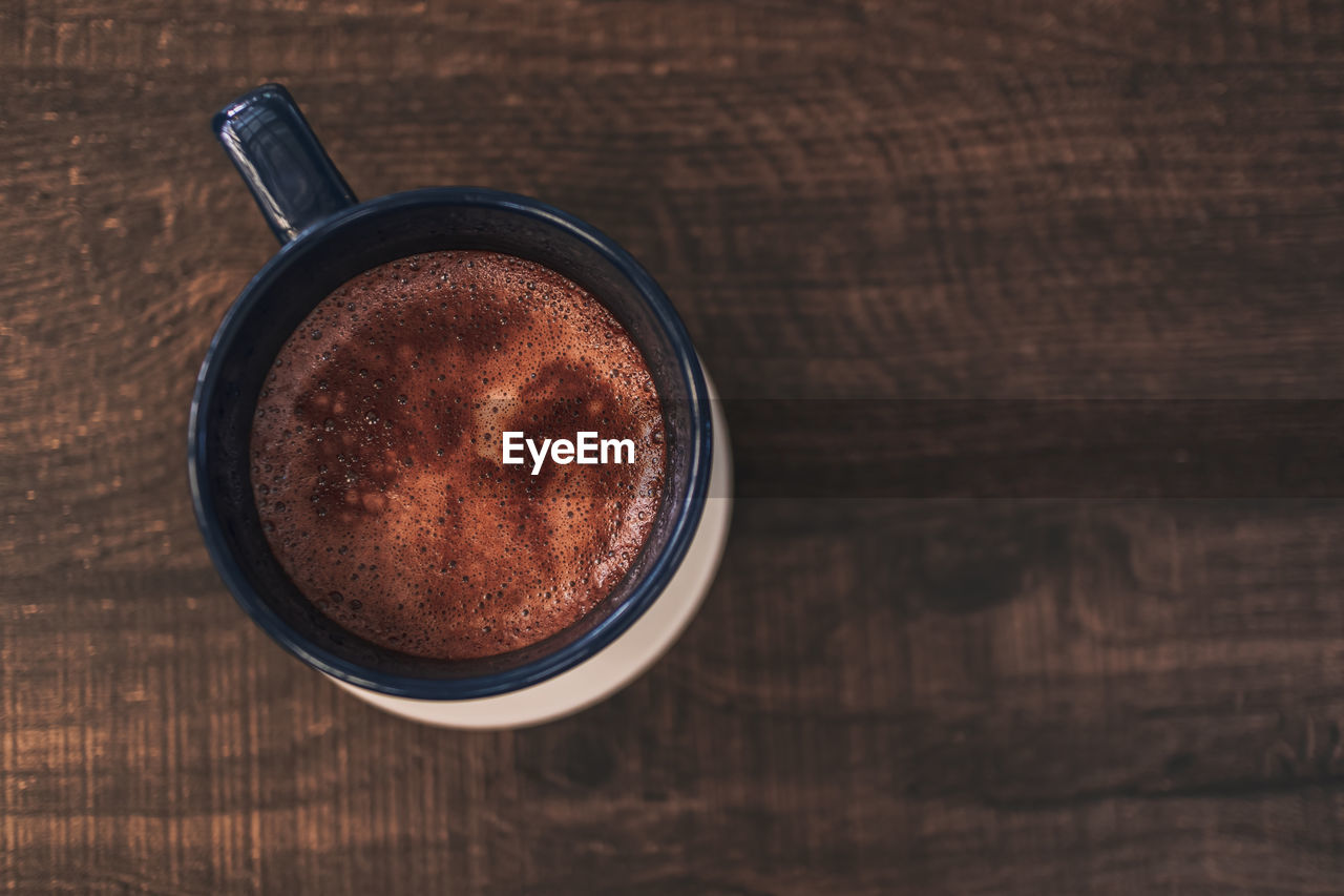 Closeup of hot cocoa drink in blue mug on wooden table.