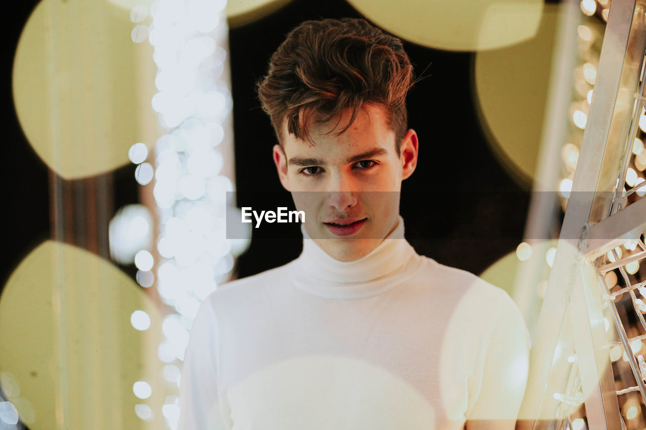 PORTRAIT OF YOUNG MAN LOOKING DOWN IN ILLUMINATED ROOM