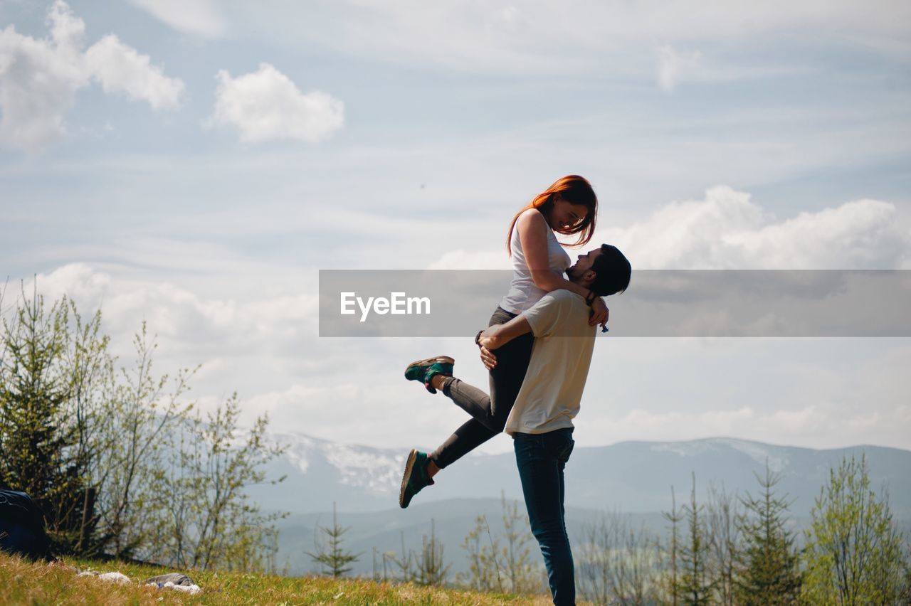 Full length of man lifting girlfriend while standing on field against sky