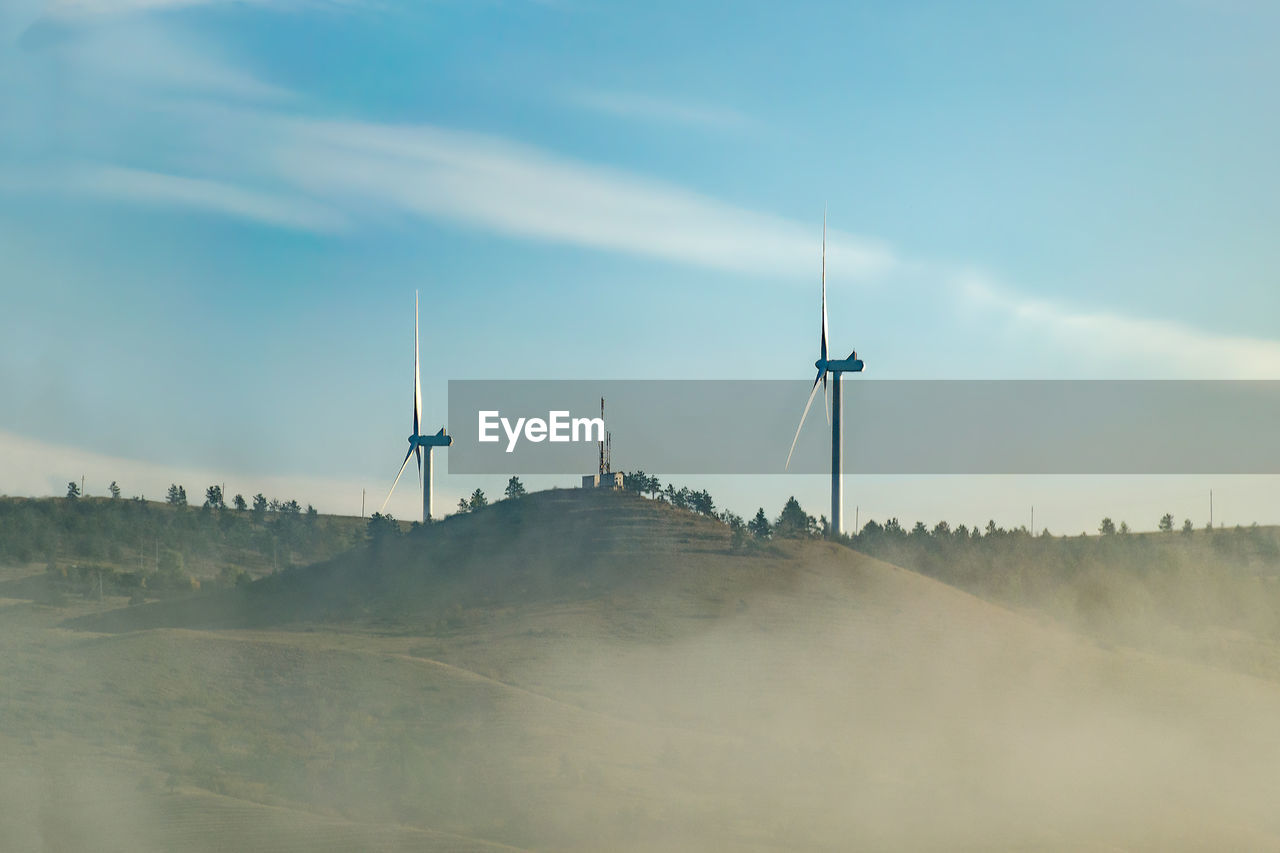 Wind farm of two wind turbine generators on top a hill, early morning, cloud of fog