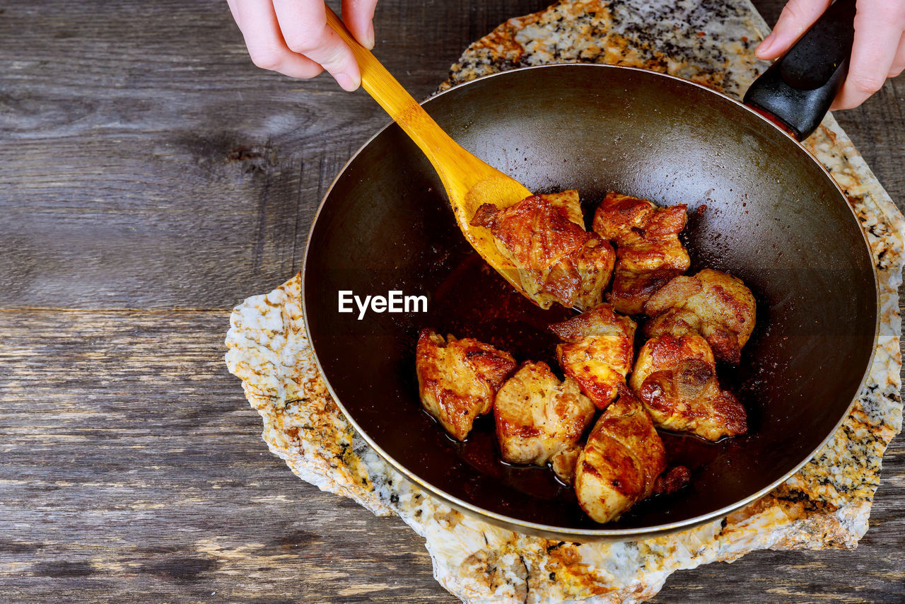 Cropped hands preparing meat in cooking pan on table