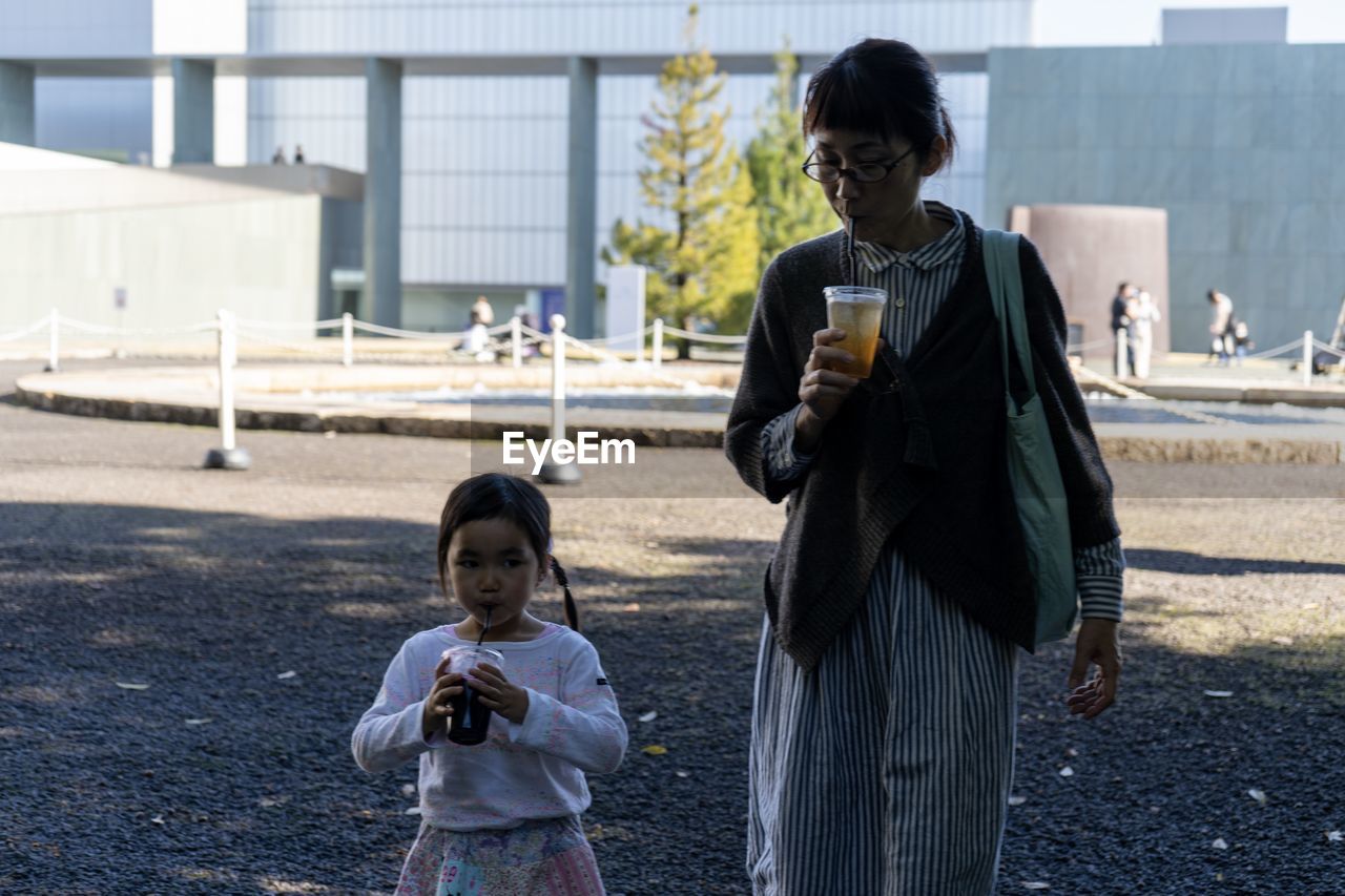 Mother and daughter having drinks while standing on road