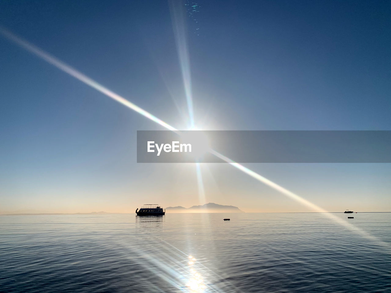 sky, water, horizon, nature, sea, sunlight, beauty in nature, sun, vehicle, transportation, blue, nautical vessel, scenics - nature, sunbeam, mode of transportation, environment, travel, tranquility, horizon over water, lens flare, reflection, ocean, no people, clear sky, outdoors, astronomical object, sunrise, tranquil scene, dawn, ship, sunny, cloud, day, idyllic, light