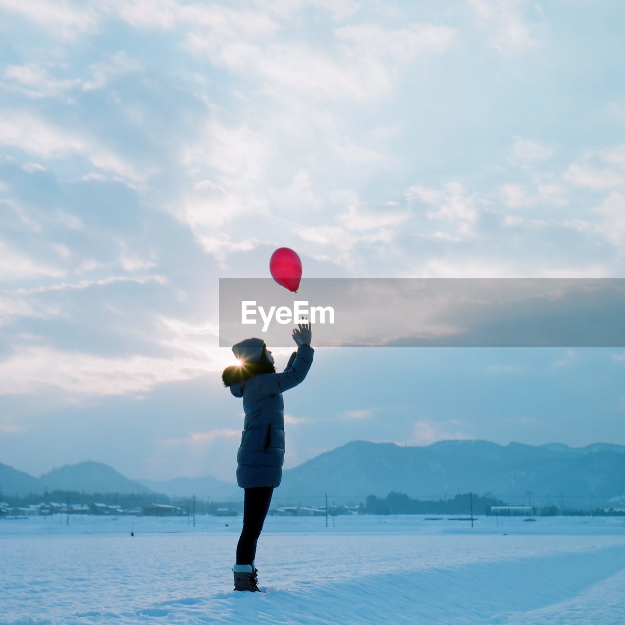 Side view of girl in warm clothing catching red balloon while standing on snowy field