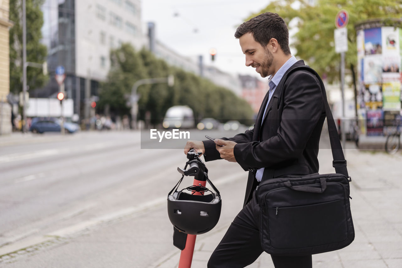 Businessman with e-scooter using cell phone in the city