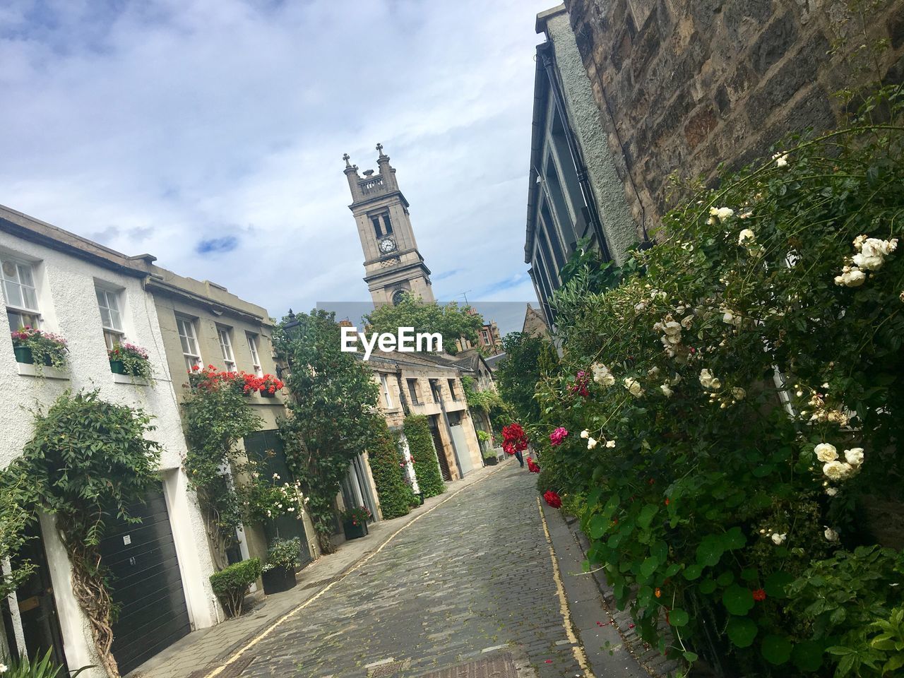 FOOTPATH AMIDST BUILDINGS AGAINST CLOUDY SKY