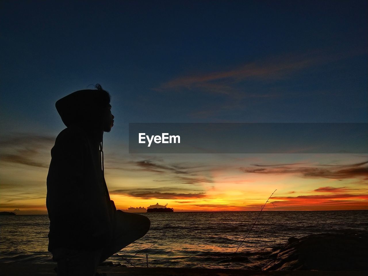 Silhouette man crouching on beach against sky during sunset