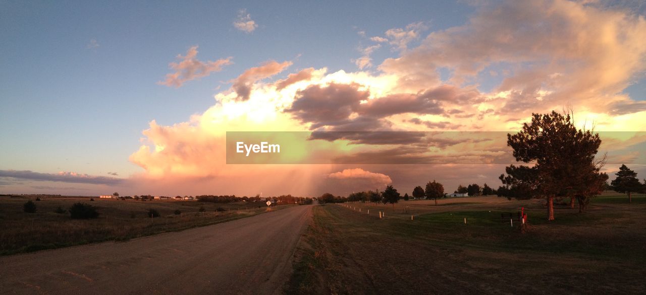 ROAD PASSING THROUGH FIELD AGAINST CLOUDY SKY AT SUNSET