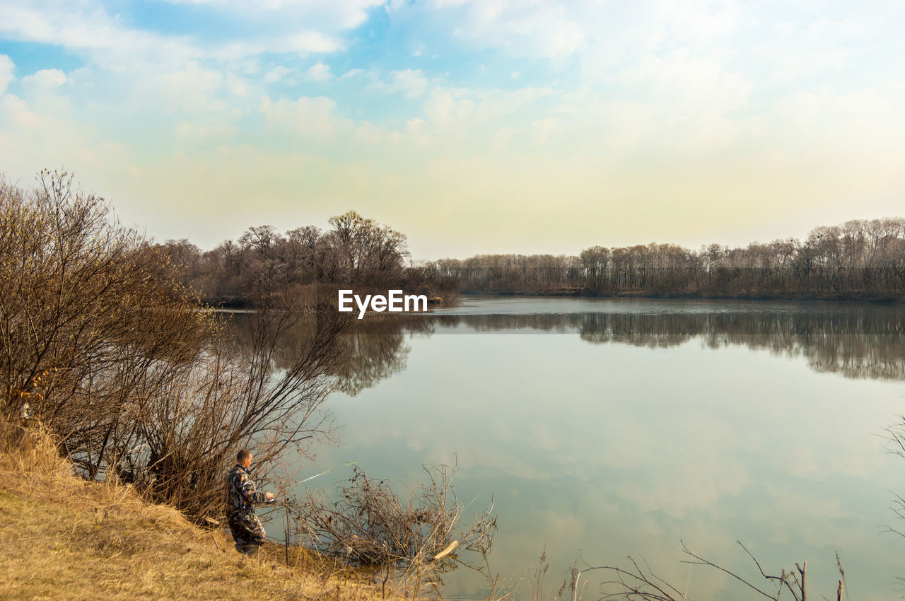 Scenic view of lake with man standing on grass against sky