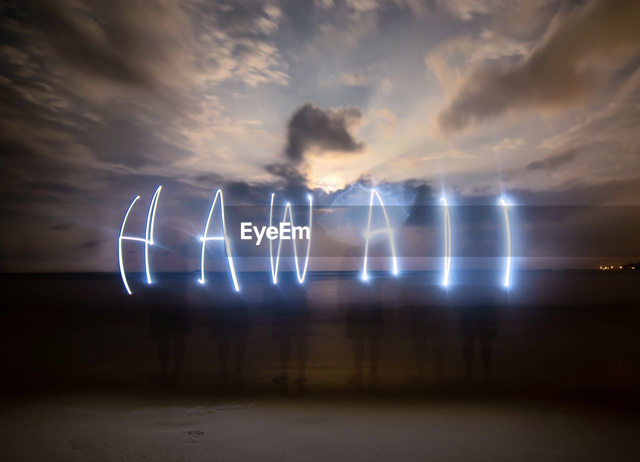 Friends making hawaii text through lights at beach during sunset