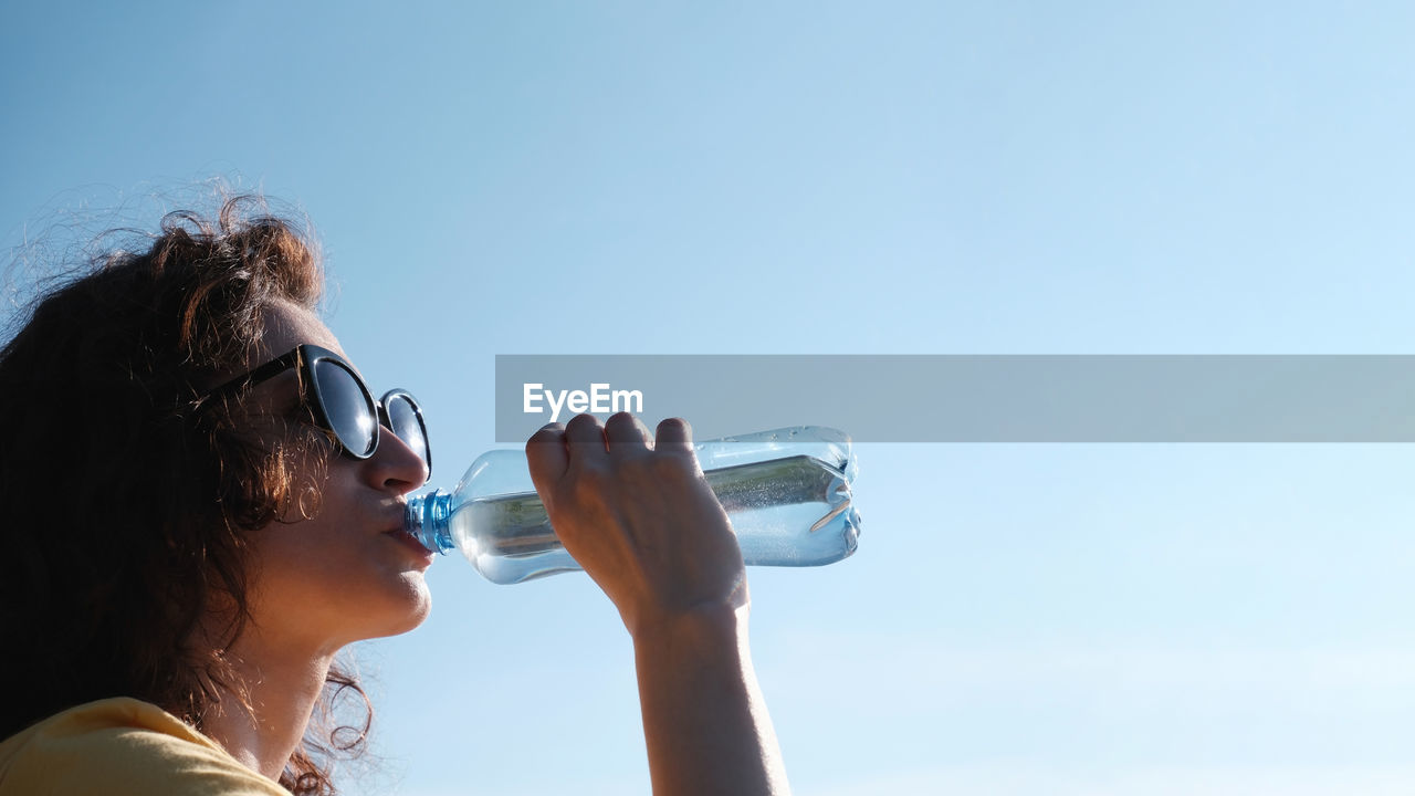Girl with glasses drinks water from a bottle in hot weather.