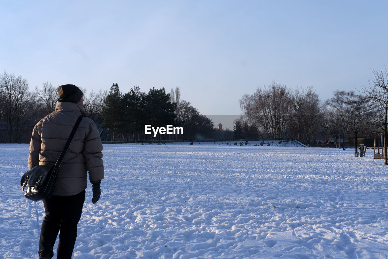 REAR VIEW OF MAN ON SNOW COVERED FIELD